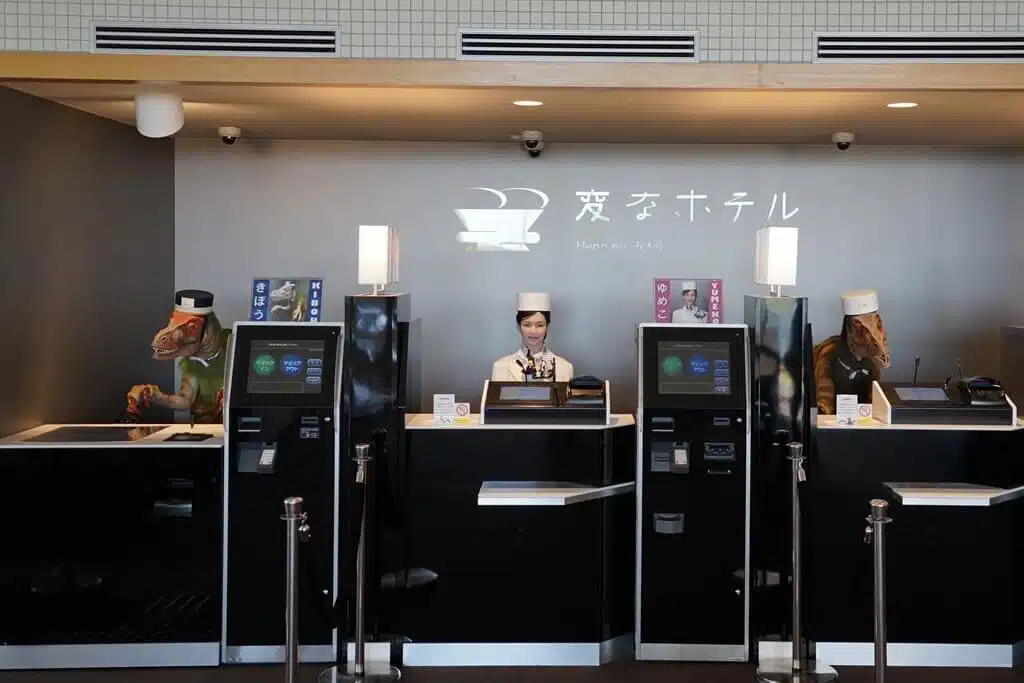 تصویری از هتل هوشمند هن نا در ژاپن است که در آن ربات ها در پشت میز قرار دارند.