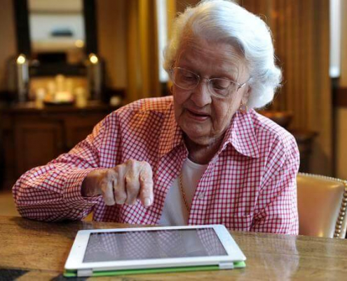 تصویری از یک زن سالمند در حال کار با تبلت جهت مدیریت خانه هوشمند برای سالمندان
