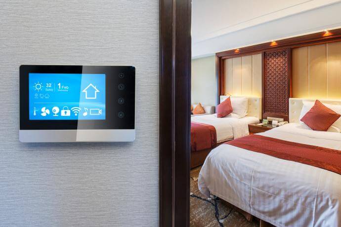 تصویری از یک اتاق در هتل هوشمند را نشان می دهد که بر روی دیوار پنل لمسی قرار دارد.