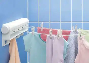 تصویر رخت آویز دیواری پلاستیکی به رنگ سفید است که داری رنگ پس زمینه آبی است و چند لباس روی آن پهن شده است.