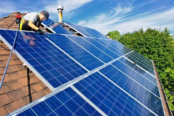 تصویری از یک مرد که پنل های خورشیدی را روی سقف خانه نصب می کند. 