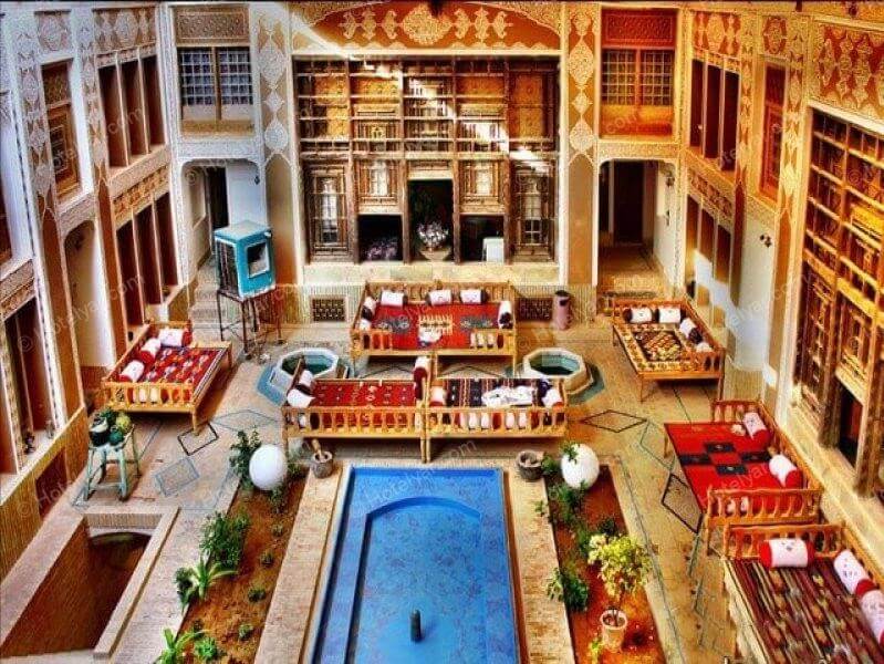 تصویری از هتل ملک التجار در یزد نشان می دهد که در وسط این هتل حوض و در اطراف آن تعدادی تخت وجود دارد.