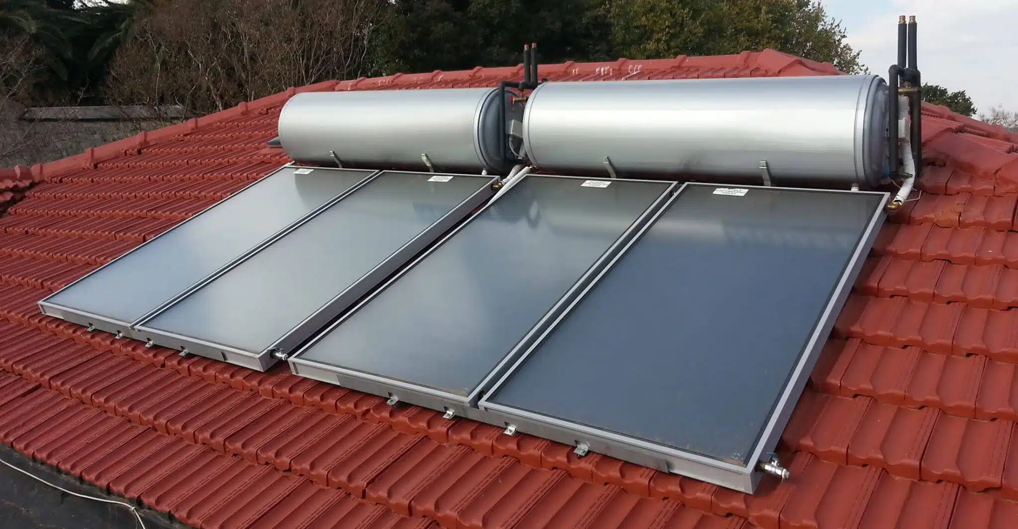 تصویری از آبگرمکن های خورشیدی که به وسیله صفحات تخت کلکتور پوشانده شده است. نمای سقف رنگ قرمز دارد 