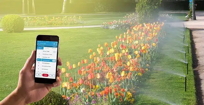 تصویری از سیستم هوشمند آبیاری را نشان می دهد که در حال آبدهی به گل ها در فضای سبز می باشد.