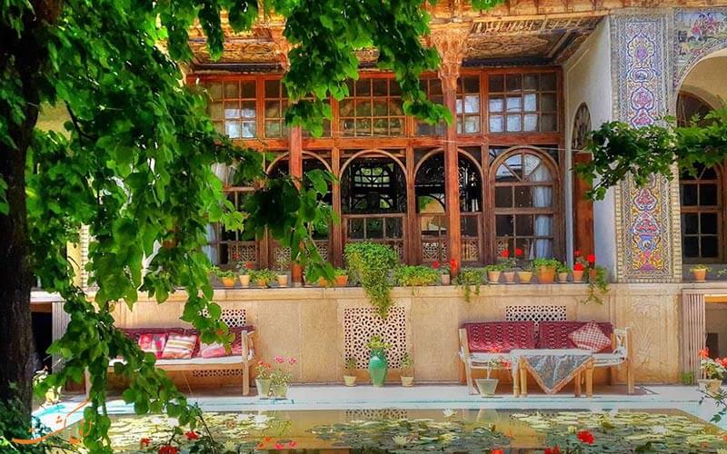 تصویری از یک خانه قدیمی در شیراز است که درب و پنجرره های چوبی به همراه یک حیاط بزرگ دارد.